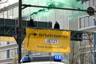 Im Design eines Landstraßenschildes hängt ein Transparent über einem Bremer Autobahnzubringer. Es signalisiert einne Abzweig zur Verkehrswende