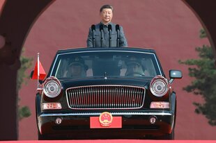 Xi Jinping steht in seinem Mao-Anzug in einer offenen Limousine die frontal aufgenommen wurde