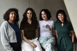 Foto von vier Frauen vor einer grauen Betonwand. Katja außen links und Anna außen rechts stehen, leicht seitlich eingedreht, während Shayna und Donata auf etwas sitzen. Sie sind Teil des neuen Teams.