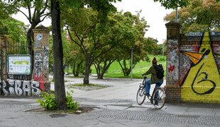 Eine Fahrradfahrerin fährt durch einen Eingang in den Görlitzer Park.