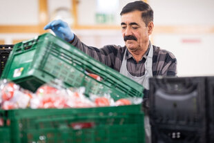 in 60-jähriger Mann mit schwarzen Haaren, Schnurrbart und kariertem Hemd stapelt Lebensmittelkisten.
