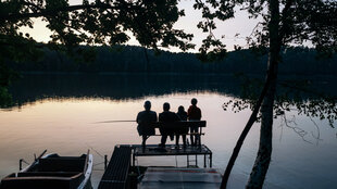 Abendstimmung, mehrer Personen sitzen an einem See auf einem Steg.