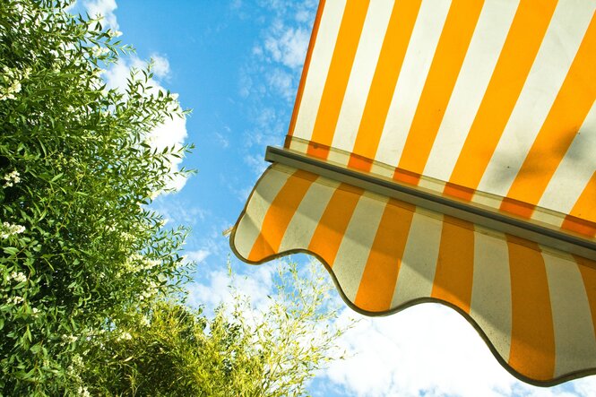 Das Foto zeigt eine rot-weiß gestreifte Markise vor sommerlichem Himmel