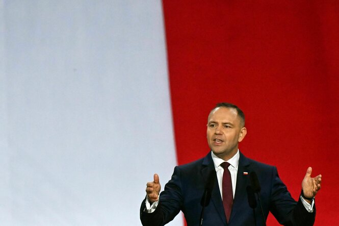 Der polnische Präsident Karol Nawrocki spricht während einer Zeremonie vor einem vertikale weiß-rot geteilten Hintergrund, die Arme erhoben