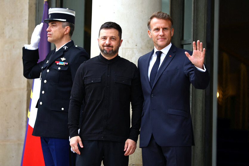 Emmanuel Macron (r), steht mit Wolodymyr Selensky im Eingangsbereich, hinter ihnen steht ein Soldat und salutiert