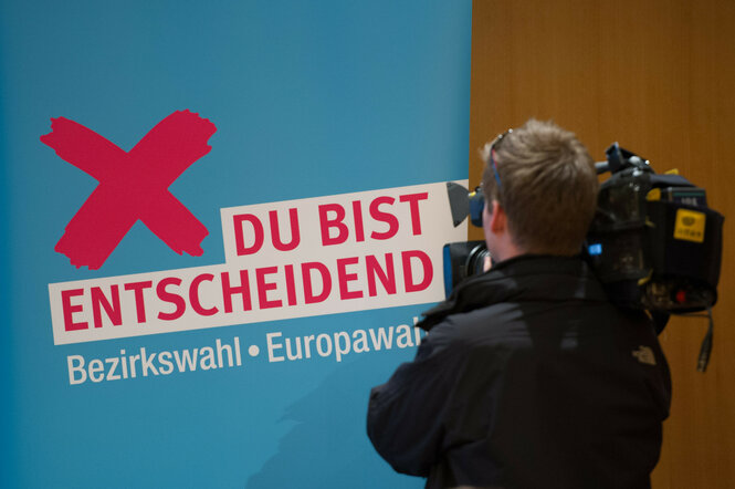 Ein Kameramann filmt einen Schriftzug mit rotem Kreuz daneben