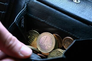 Eine Hand greift in einen Geldbeutel mit Münzen