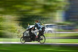 Frau auf einem Lastenrad mit Kindersitz faehrt auf einer Straße