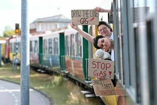 Aktivist:innen demonstrieren gegen Gasbohrungen vor Borkum und halten Protestschilder aus einem Zug
