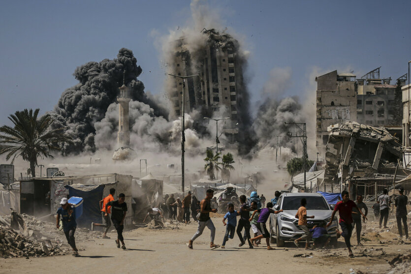 Im Hintergrund fällt ein bombardiertes Hochaus ein, davor rennen Menschen