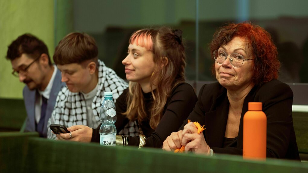 Vier Personen sitzen nebeneinander, eine von ihnen schaut verzagt