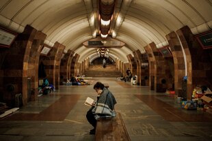 Eine Frau in Charkiw sitzt in einer U-Bahnstation und liest während eines russischen Bombenangriffs