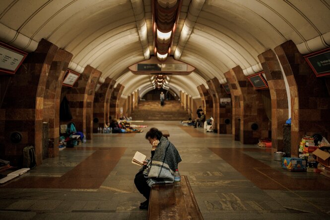 Eine Frau in Charkiw sitzt in einer U-Bahnstation und liest während eines russischen Bombenangriffs