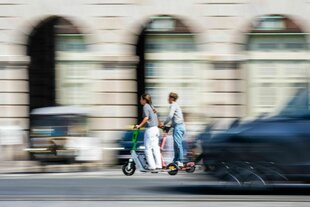 Zwei Menschen auf einem E-Scooter vor verwischtem Hintergrund