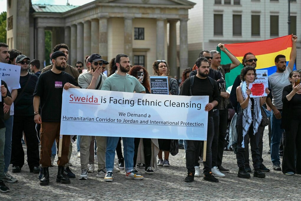Eine Gruppe von Menschen steht mit einem Transparent vor dem Brandenburger Tor und warnt mit einem Plakat vor den ethnischen Säuberungen in Suweida