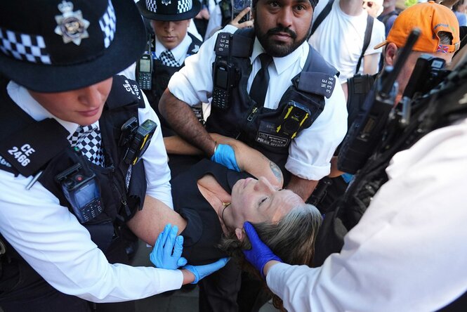 Ältere Frau wird von britischen Polizisten in Uniform weggetragen
