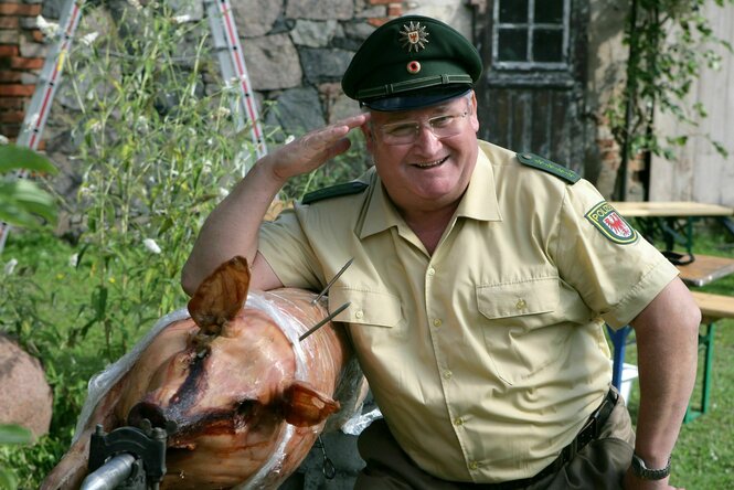 Horst Krause posiert in Polizeikostüm neben einem Spanferkel
