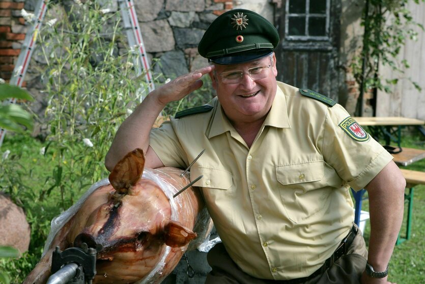 Horst Krause posiert in Polizeikostüm neben einem Spanferkel