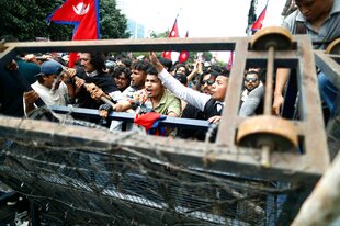 Junge Männer versuchen eine Barrikade zu durchbrechen, sie schwenken Flaggen und scheinen sehr empört zu sein