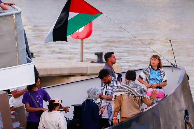 Greta Thunberg steht mit anderen Aktivisten an Bord eines Schiffes. Eine palästinensiche Flagge weht und viele tragen eine Pali-Tuch um den Hals