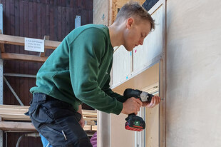 Ein Auszubildender steht vor dem Mock-Up und entfernt mit einem Akkubohrer die Verkleidung