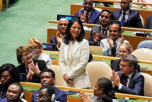 Eine Frau in einem weißen Anzug wird von anderen Personen beklatscht