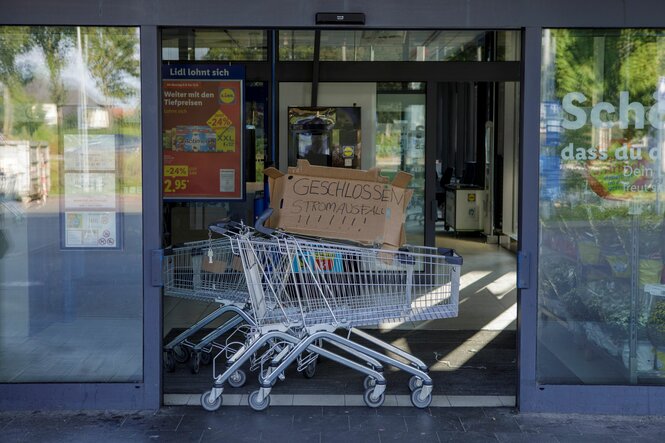 Im Eingang eines Supermarkts steht ein Einkaufswagen mit einer Pappe mit der Aufschrift "Geschlossen Stromausfall".
