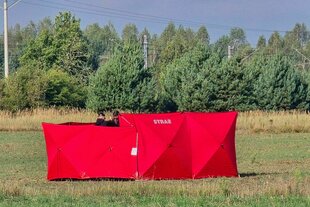 Personen arbeiten hinter rotem Sichtschutz auf einer Wiese