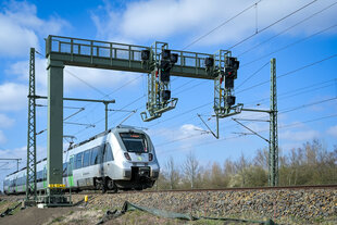 Zug der auf Schienen unter Signalbrücke hindurchfährt