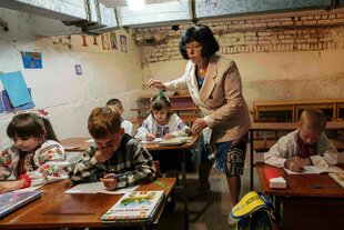 Eine Lehrerin steht im Klassenzimmer, das sich im Keller eines Gebäudes befindet, die Kinder arbeiten an ihren Tischen in Arbeitsheften