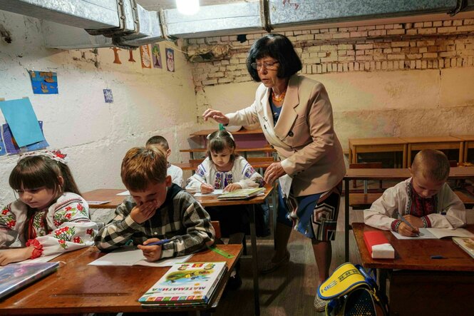 Eine Lehrerin steht im Klassenzimmer, das sich im Keller eines Gebäudes befindet, die Kinder arbeiten an ihren Tischen in Arbeitsheften
