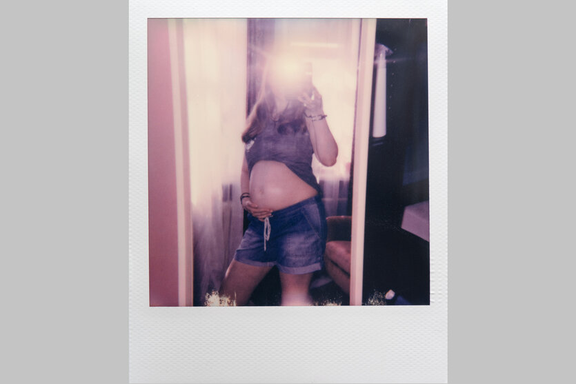 Eine junge schwangere Frau in kurzen Jeans-Hosen steht vor dem Spiegel und macht ein Selfie von sich