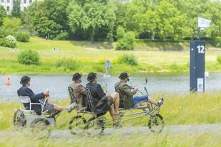 Männergruppe unterwegs im Grünen mit einem selbstgebauten Fahrgerät mit vier Plätzen - sie müssen treten