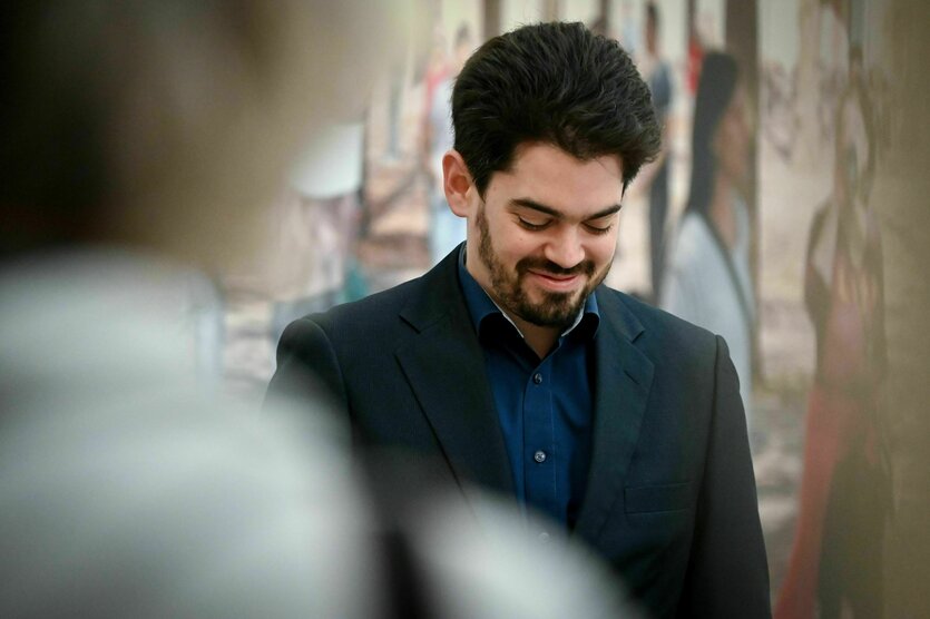 Porträt von Lahav Shani, er hat dunkle kurze Haare und trägt einen Bart, er schaut nach unten und lächelt