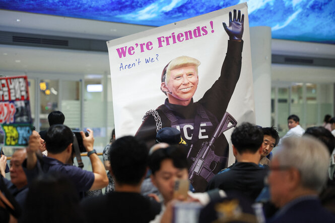 Menschen stehen am Flughafen in einer Menge, einer hält ein Plakat hoch auf dem Donald Trump abgebildet ist mit der Frage "We´re Friends! Aren´t we ?