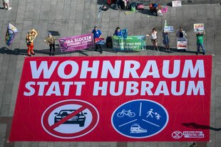 Bild aus der Vogelperspektive von Protest gegen die IAA. Auf einem Banner steht "Wohnraum statt Hubraum"