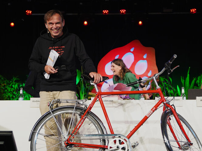 Hermann-Josef Tenhagen mit einem taz Rad auf der Bühne