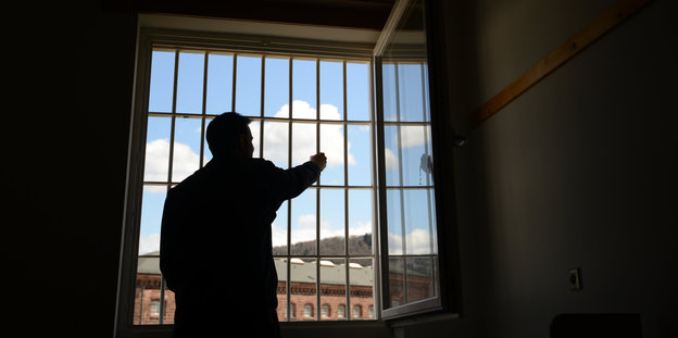 Ein Mann steht an einem vergitterten Fenster