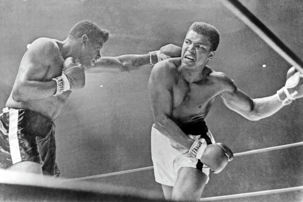 Muhammad Ali bewegt sich auf seinen Gegner zu, dessen ausgestreckte Faust knapp neben seinem Kopf zu sehen ist