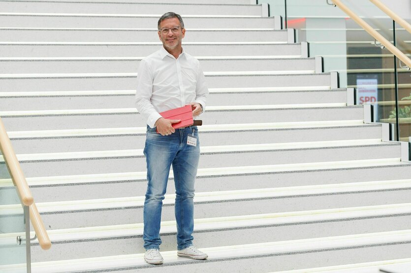 Marc Herter steht in Jeans und Hemd vor einer hellen Treppe