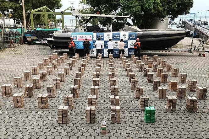 Stapel mit beschlagnahmten Kokain-Paketen an Land vor einem Schnellboot