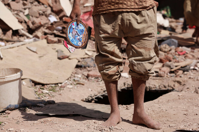 Ein Mann steht mit dem Bild eines Jungen in der Hand vor einem zerstörten Haus in Sanaa