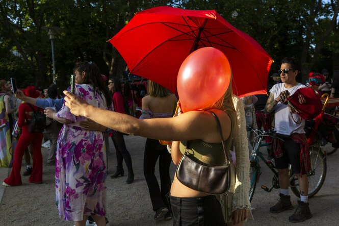 Demonstration, eine weibliche gelesene Person, deren Gesicht durch einen rotne Luftballon verdeckt ist und unter einem roten Regenschirm steht