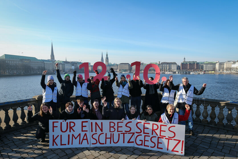 Menschen stehen an der Alster in Hamburg, auf einem Transparent vor ihnen steht: Für ein besseres Klimaschutzgesetz. Einige halten Zahlen hoch, ein Datum: 12.10.