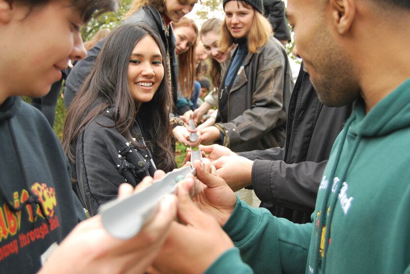 junge Menschen lassen eine Murmel durch gemeinsam nebeneinander gehaltene Rohre rollen