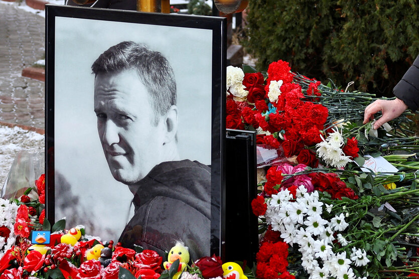 Blumen liegen rund um ein schwarz gerahmtes Foto von Alexei Navalny