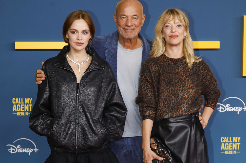 Ein älterer Mann umarmt zwei jüngere Frauen