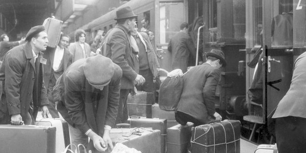 Viele Männer stehen vor einem Zug und sammeln ihre Koffer, um einzusteigen