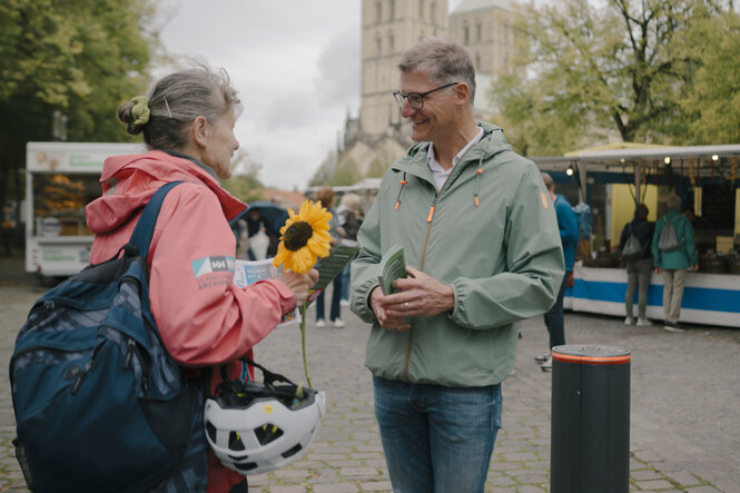 Mann unterhält sich auf einem Marktplatz mit einer Frau