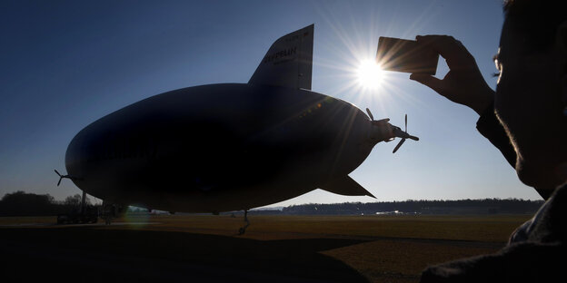 Ein Zeppelin im Gegenlicht wird mit einem Smartphone fotografiert